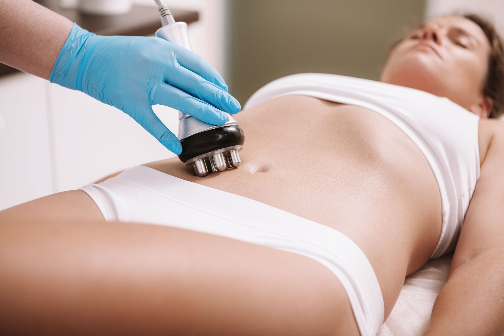 Gloved hand using a handheld device on a woman’s abdomen during a body treatment