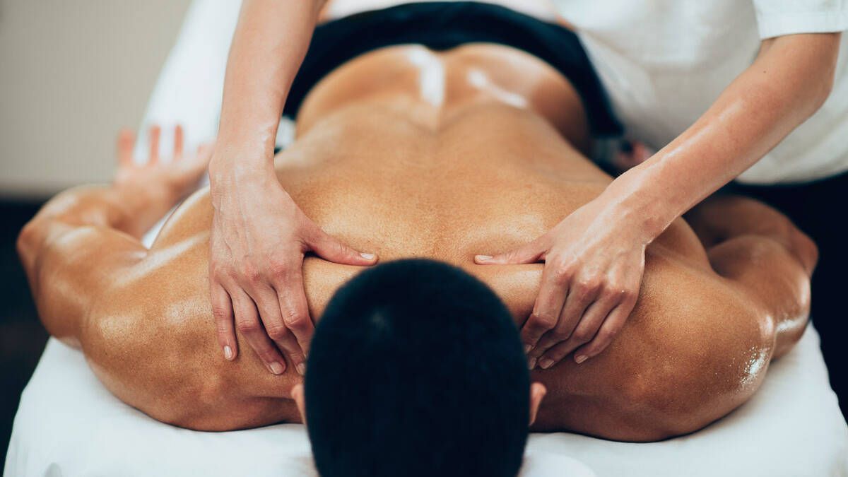 Two hands massage the shoulders and upper back of a person lying face down on a spa table.