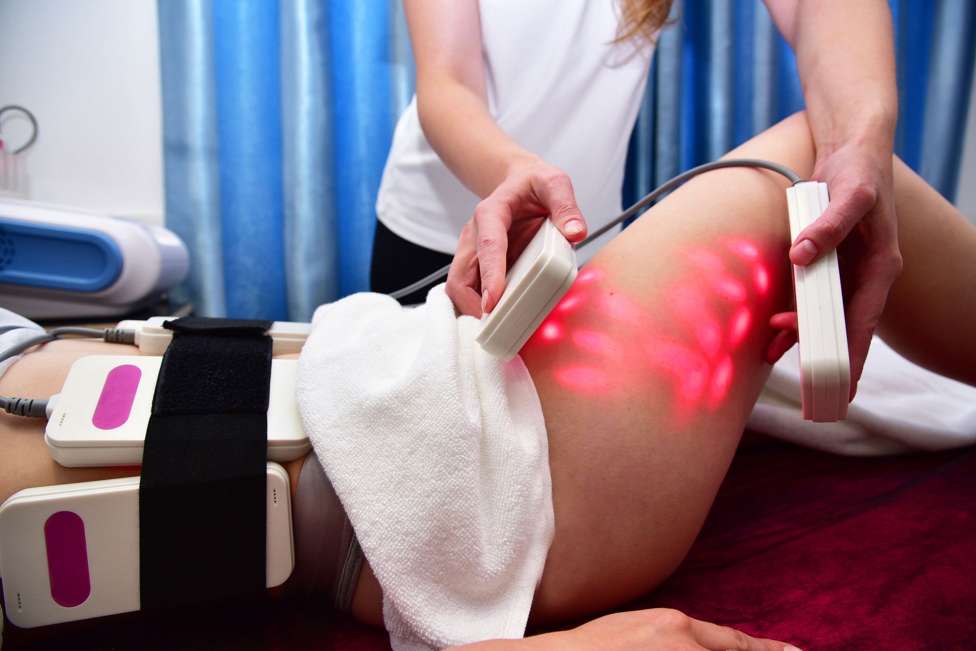 Physical therapy device being applied to a leg, with red light treatment on the thigh in a clinic.