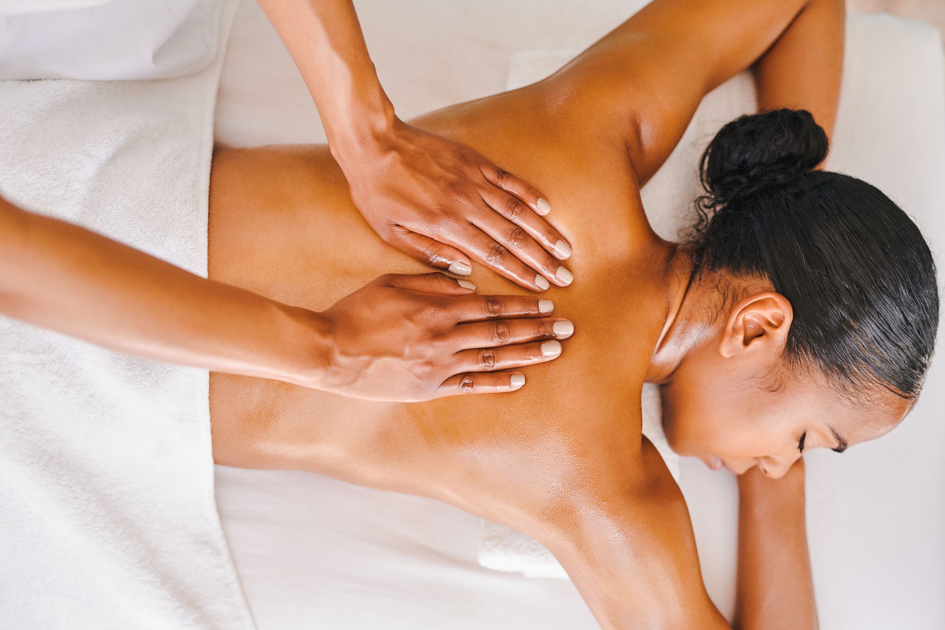 Massage therapist kneading a woman's back on a spa table, with warm lighting and white towels