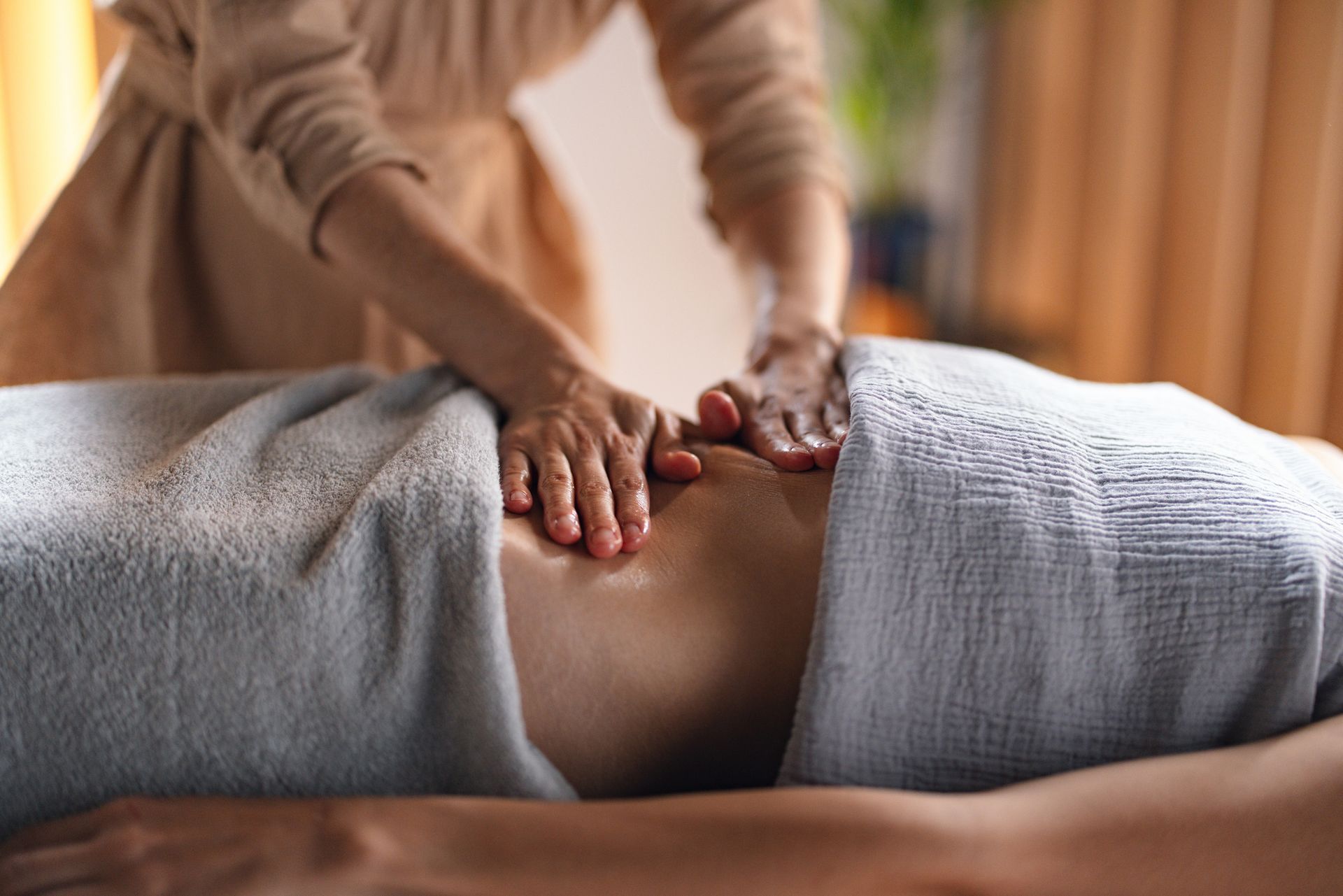 Hands massage the back of a person lying on a table, covered with white towels.