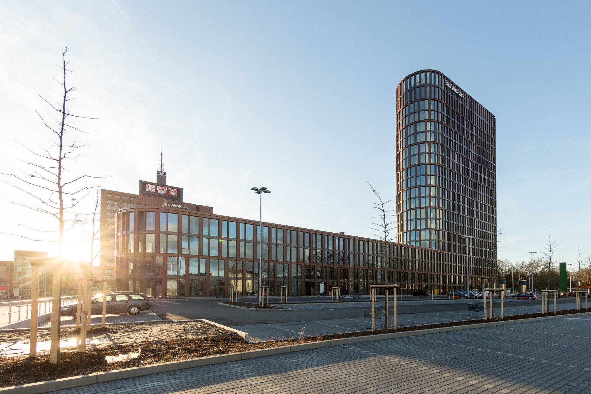 Ein großes Gebäude mit vielen Fenstern ist von Bäumen und einem Parkplatz umgeben.