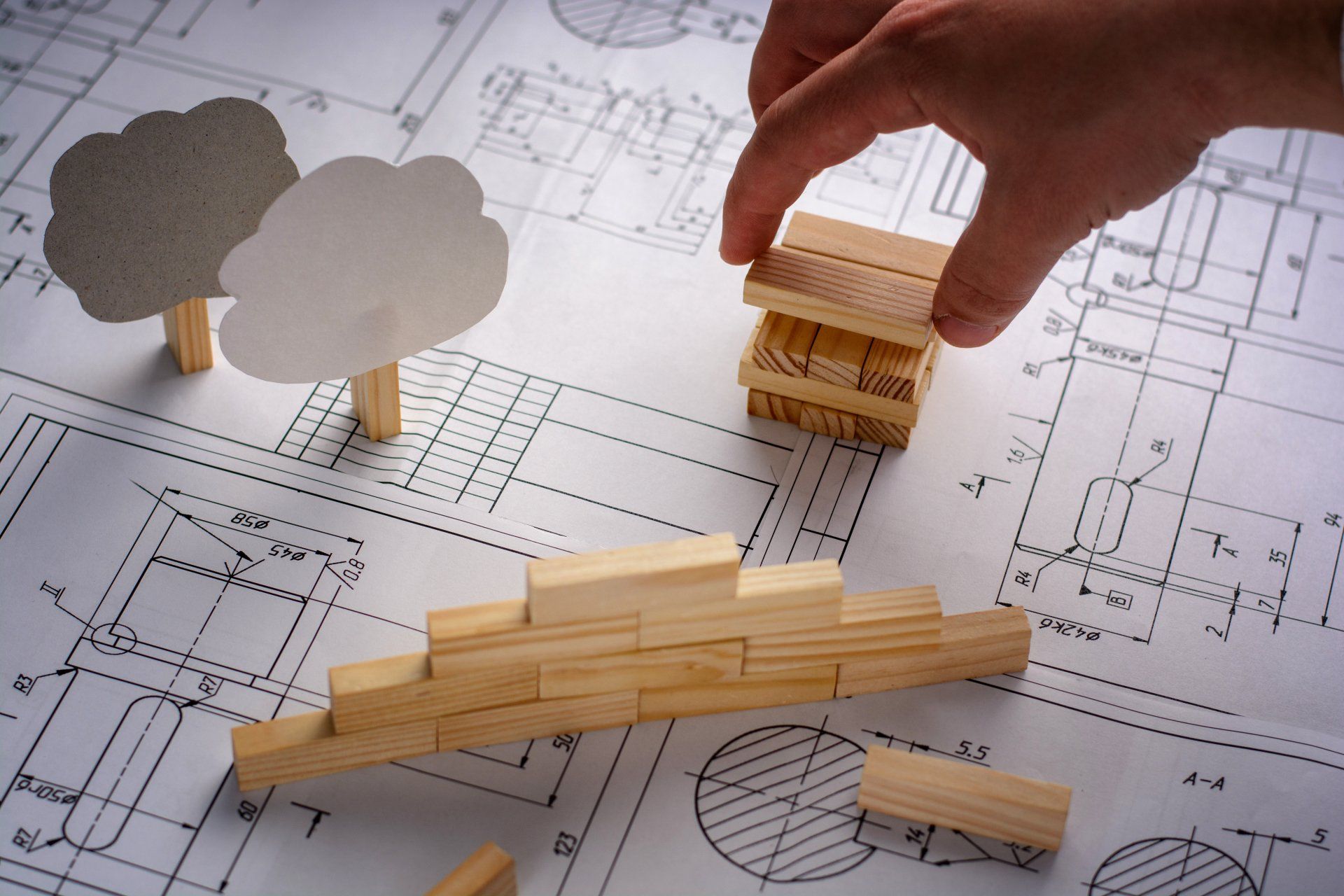 Eine Person spielt mit Holzklötzen auf einem Bauplan.