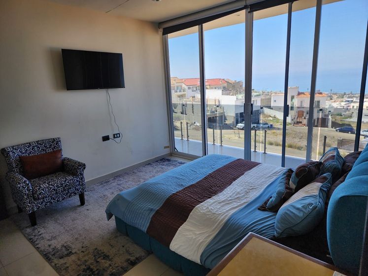 A bedroom featuring a blue bed with brown accents, a patterned armchair, and wall-mounted TV for Ibogaine treatment