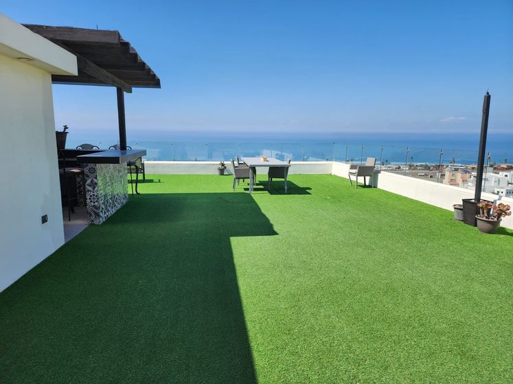 A rooftop terrace with artificial turf, a small bar, outdoor furniture, and a panoramic ocean view for Ibogaine treatment