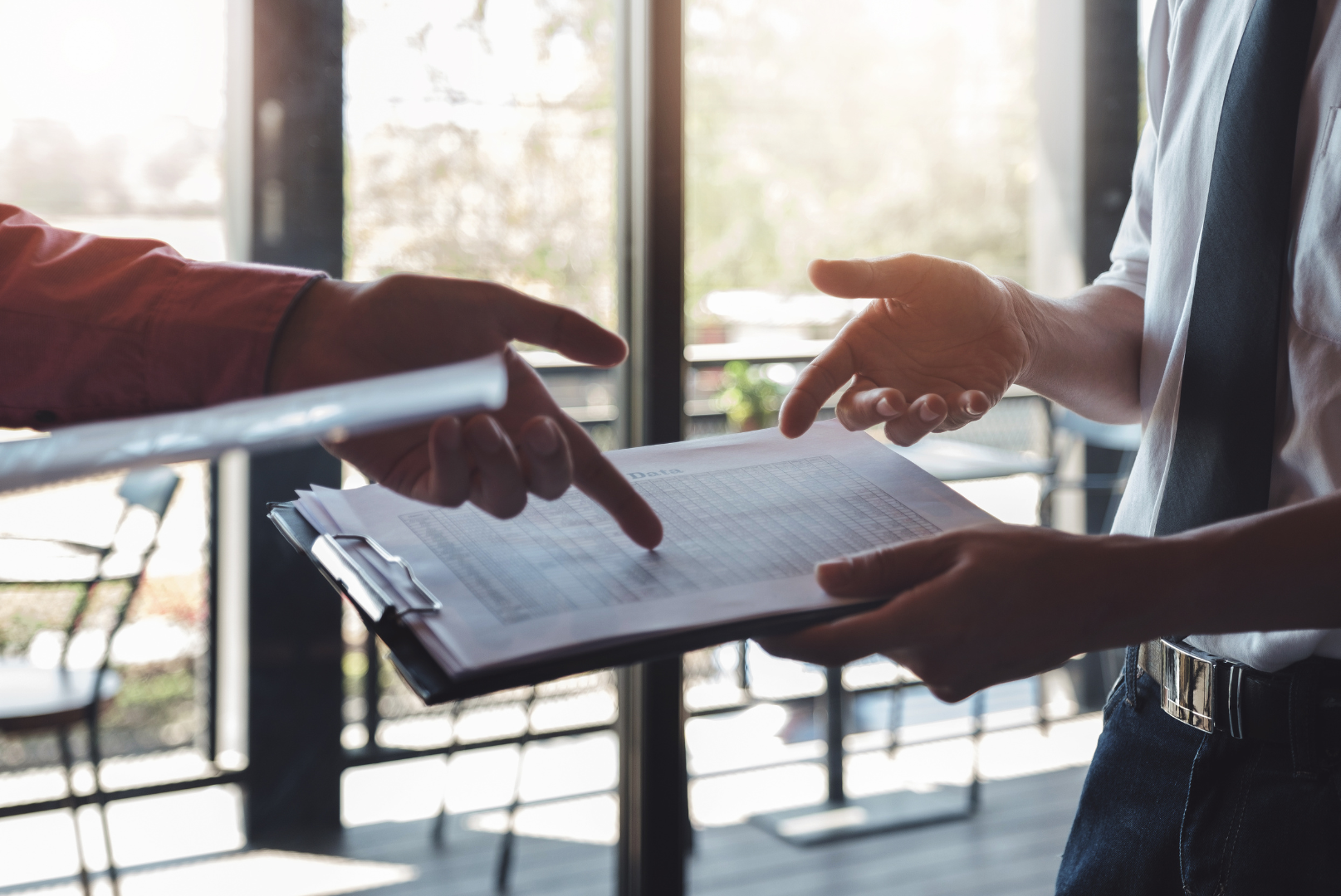 A man is pointing at a clipboard while another man holds a clipboard.