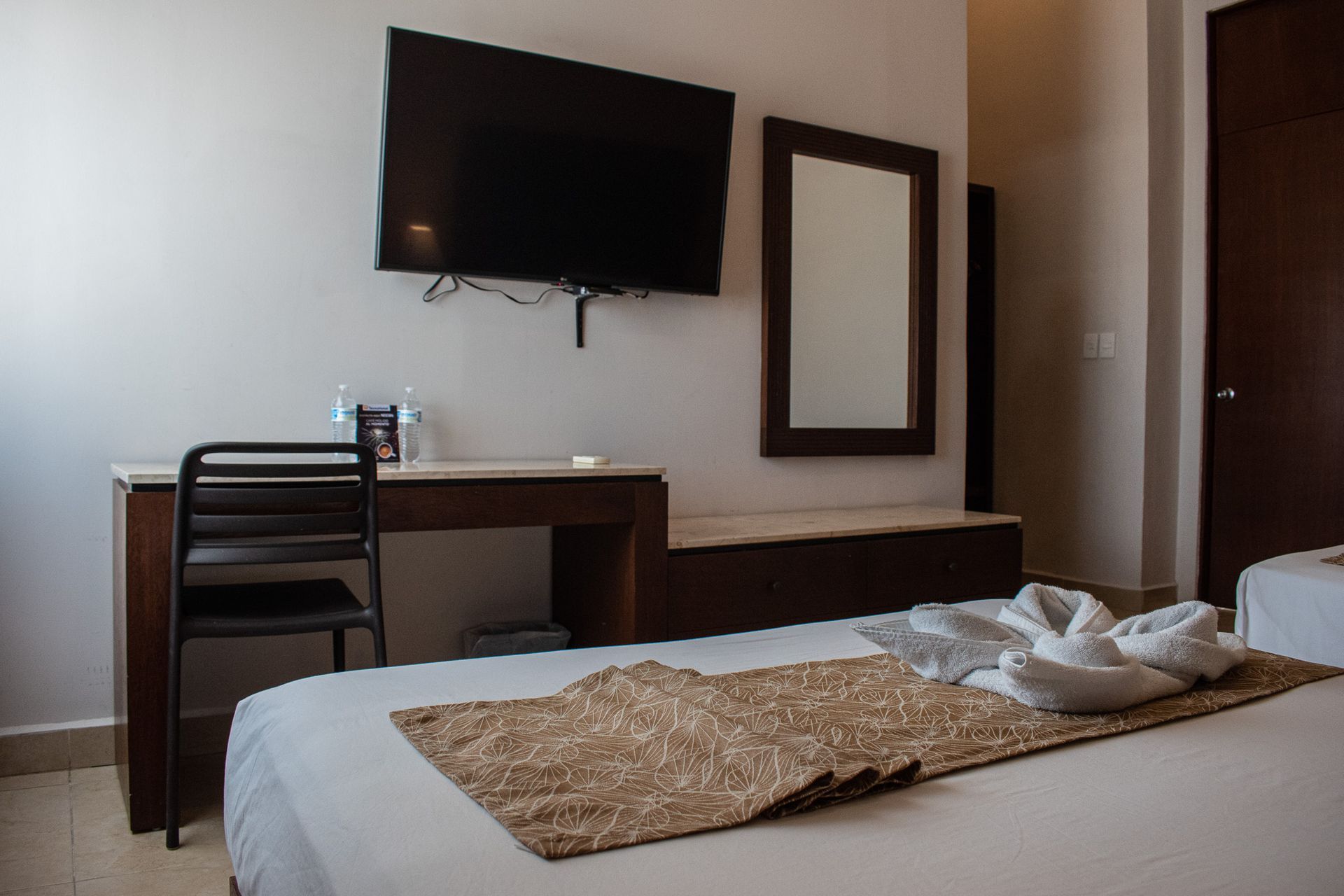 Una habitación de hotel con dos camas, un escritorio, una televisión y un espejo.