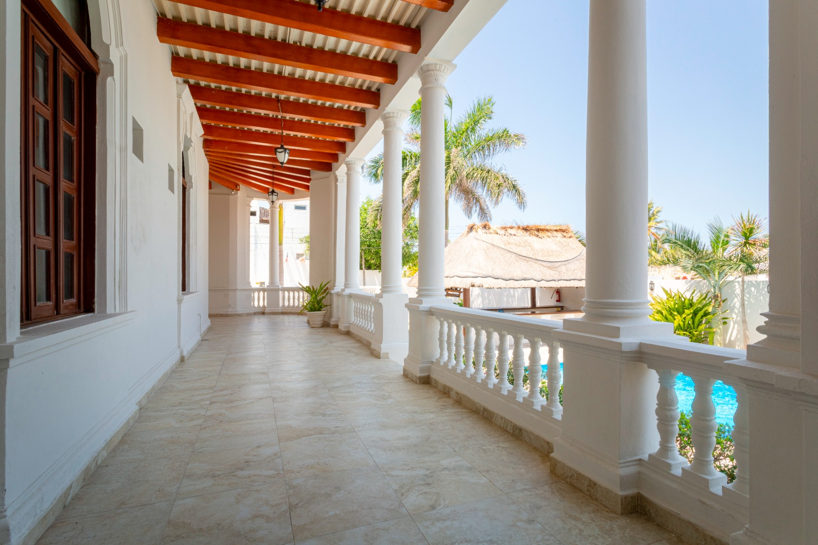Un largo pasillo blanco con columnas y un techo de madera que conduce a un balcón.