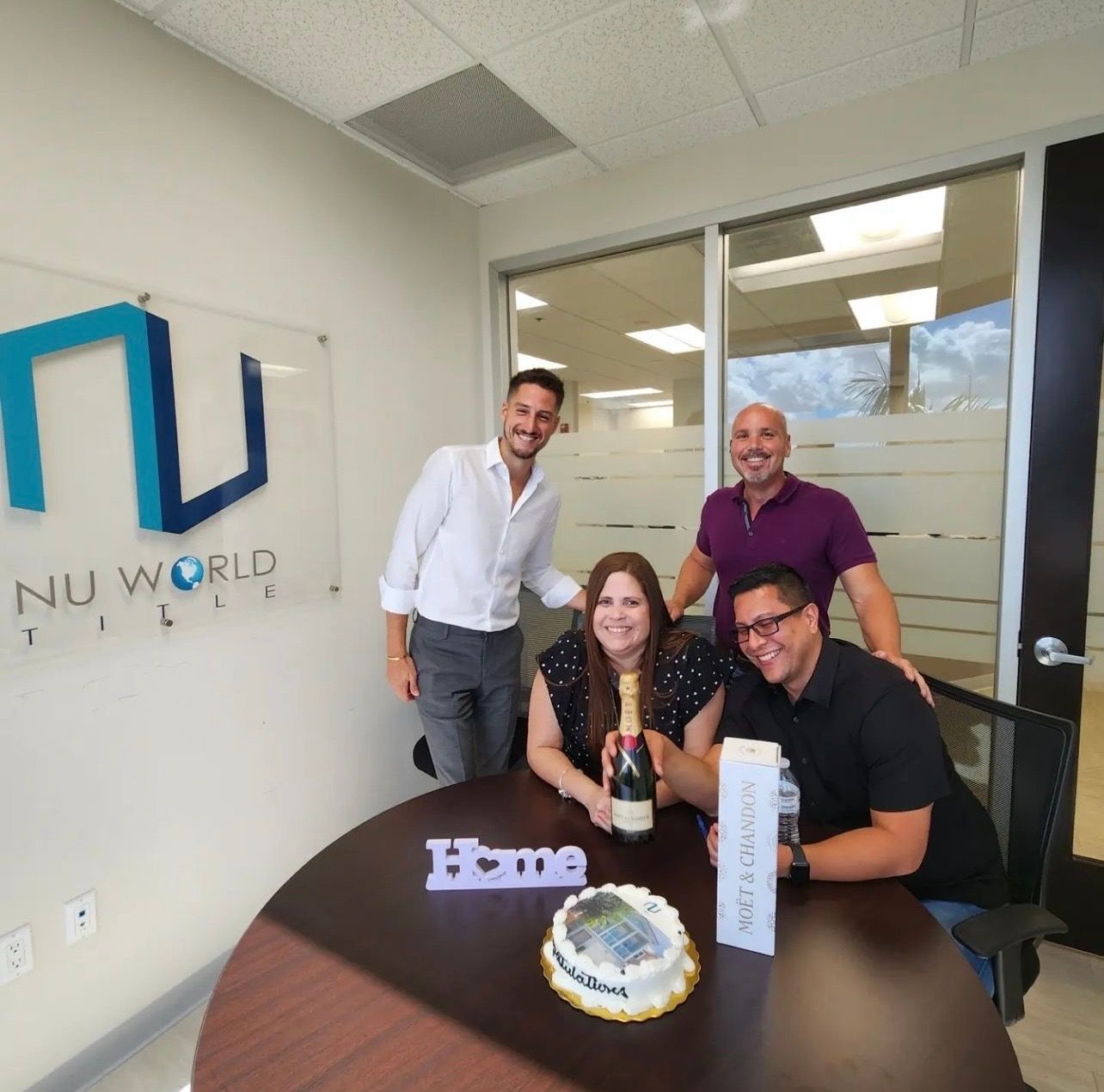 A group of people standing around a table with a cake and a sign that says home