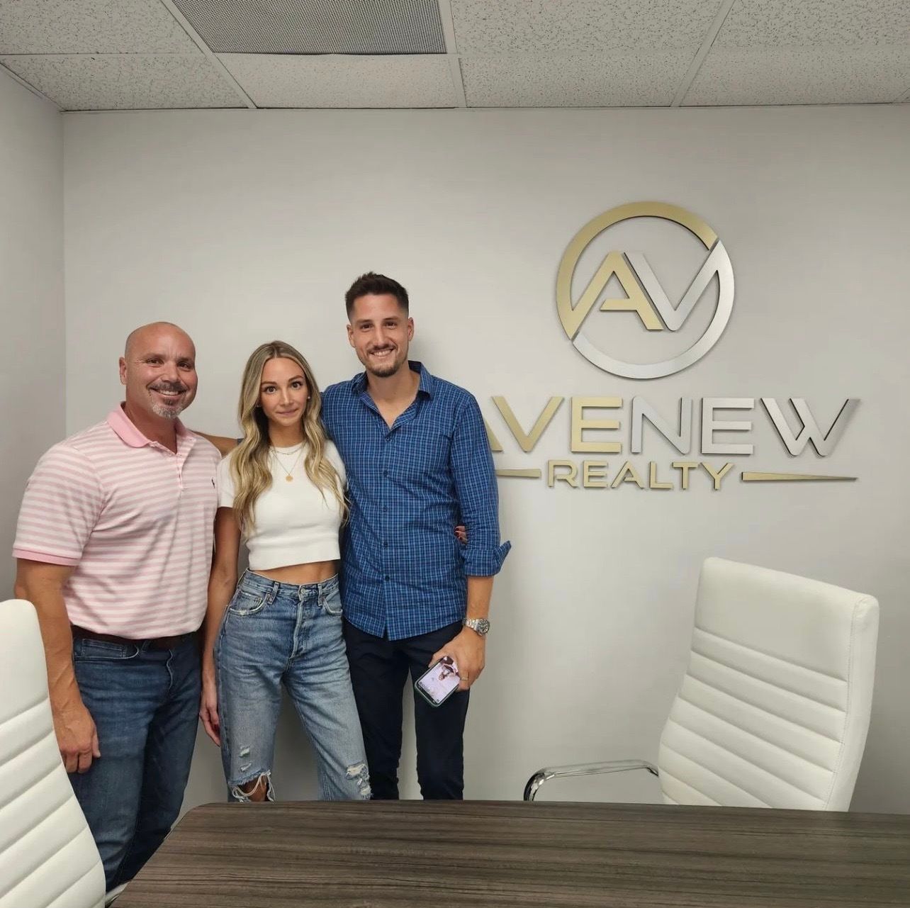 Three people pose in front of a venew realty sign