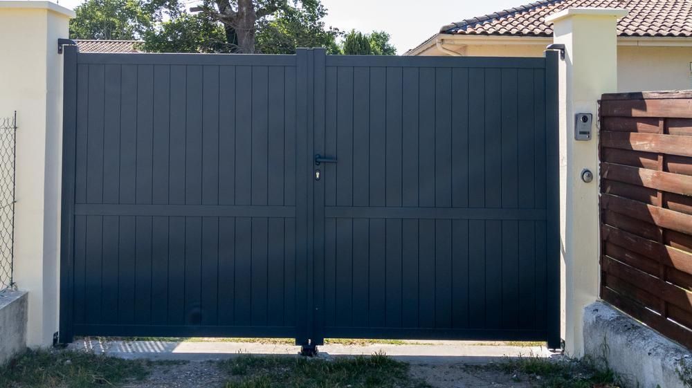 A Black Gate Is Sitting Next To A Wooden Fence In Front Of A House — Rabbo's Fencing Services In Virginia, NT