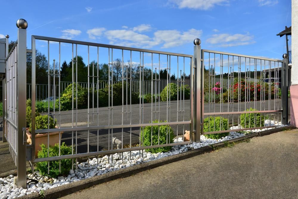 A Stainless Steel Fence With A Gate Is Surrounded By Rocks And Bushes — Rabbo's Fencing Services In Katherine, NT
