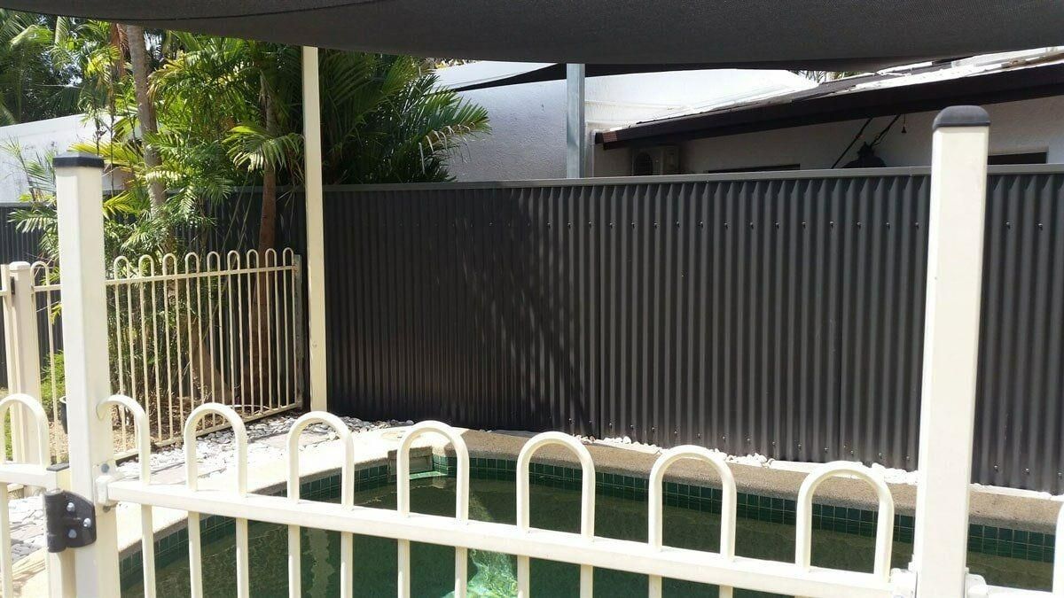 A Fence Surrounds A Swimming Pool With A Canopy Over It — Rabbo's Fencing Services In Pinelands, NT