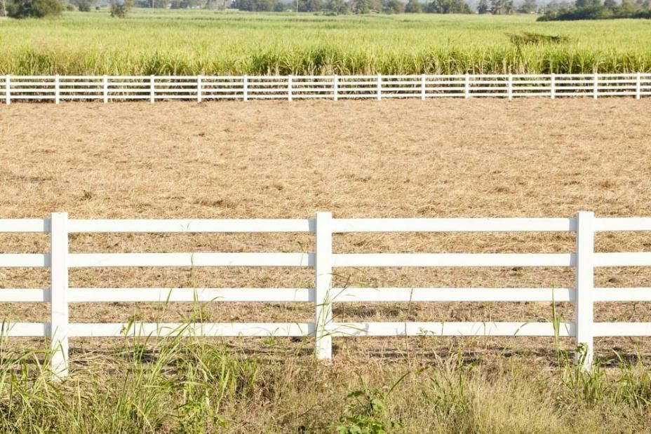 A White Fence Surrounds A Dry Grassy Field — Rabbo's Fencing Services In Pinelands, NT