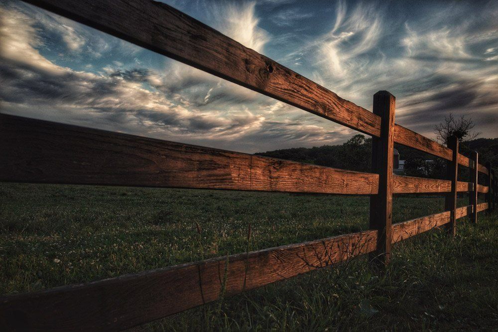 A Wooden Fence Surrounds A Grassy Field With A Cloudy Sky In The Background — Rabbo's Fencing Services In Pinelands, NT