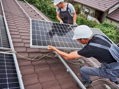 Two men are installing solar panels on the roof of a house.