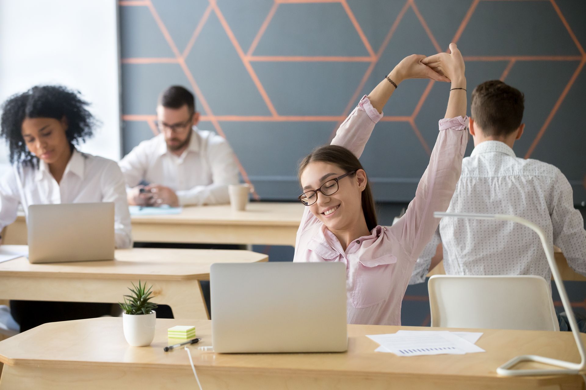 Office with colleagues. A lady in the front of the photo is happy and streching.