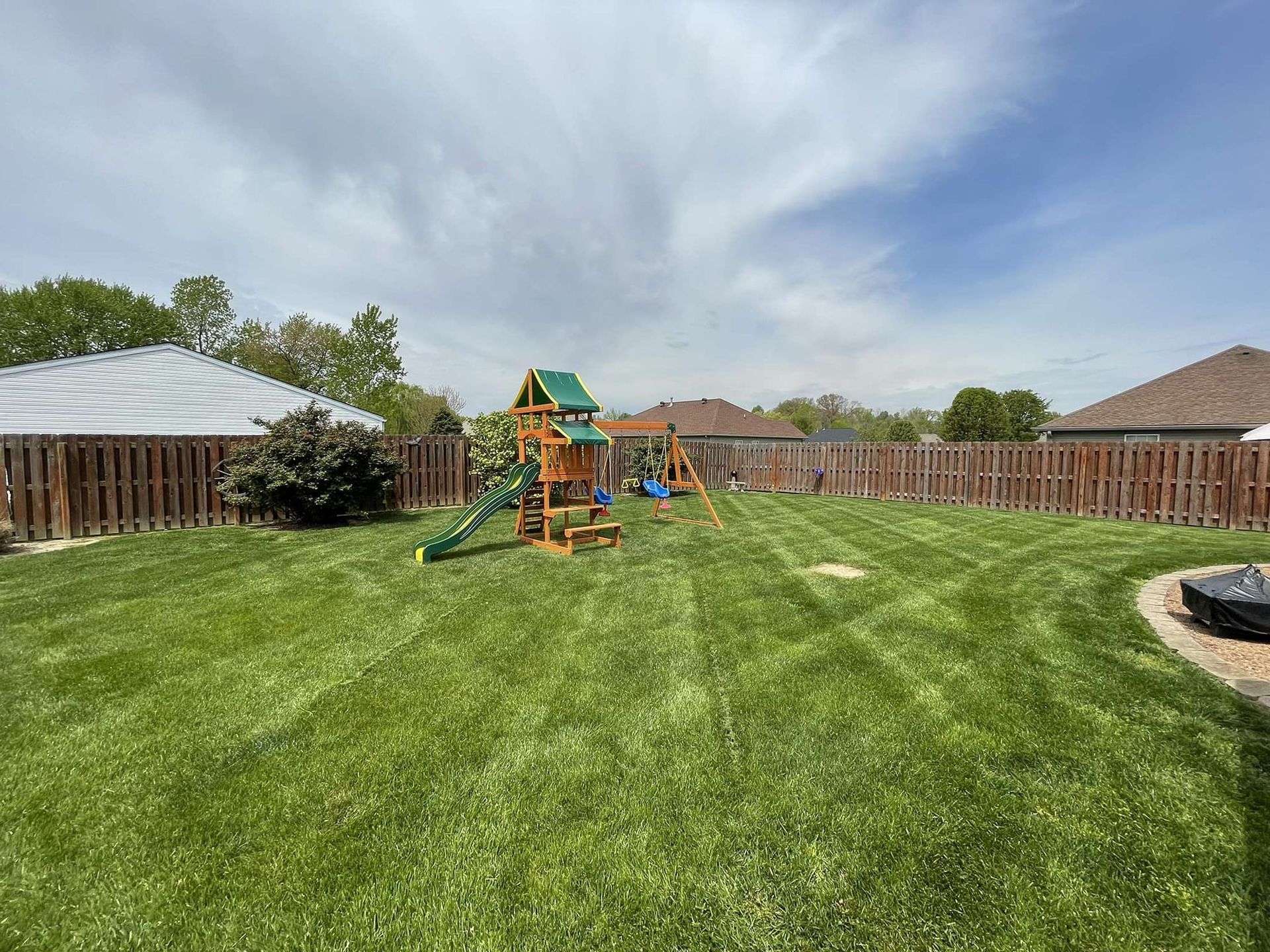 Green backyard with a wooden playset, swings, and a neatly mowed lawn.