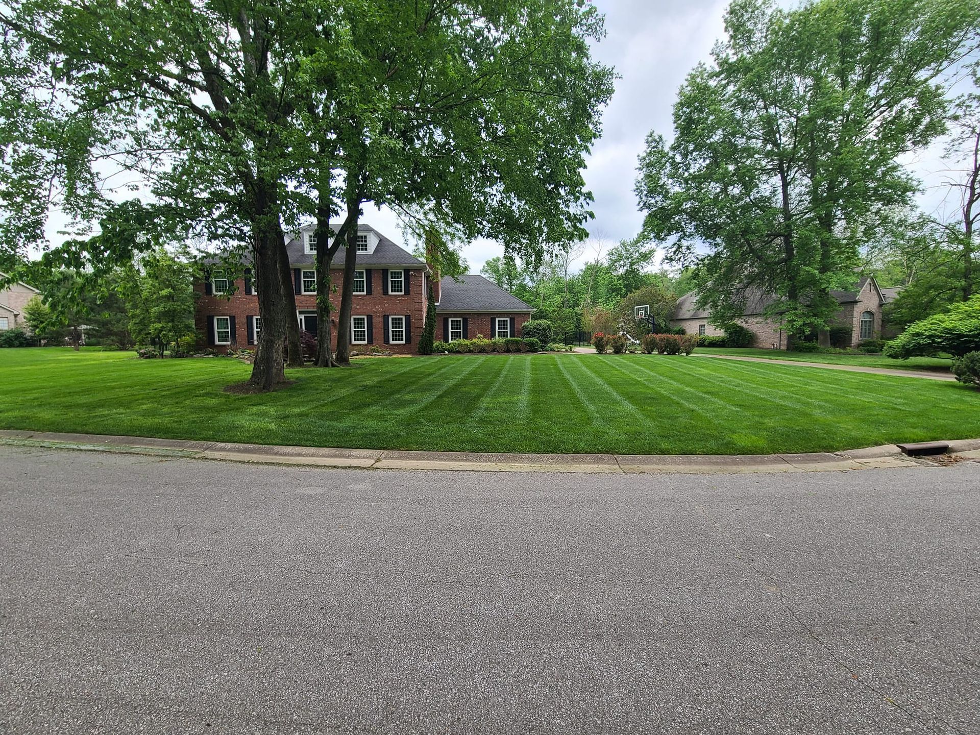 House with large lawn; mowed grass, trees, and cloudy sky.