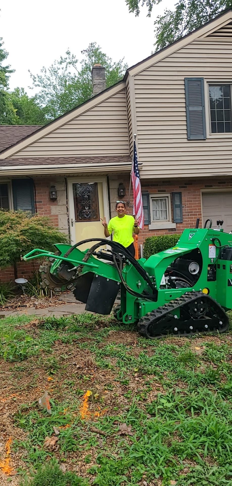 Man standing by green stump grinder in front of a house.