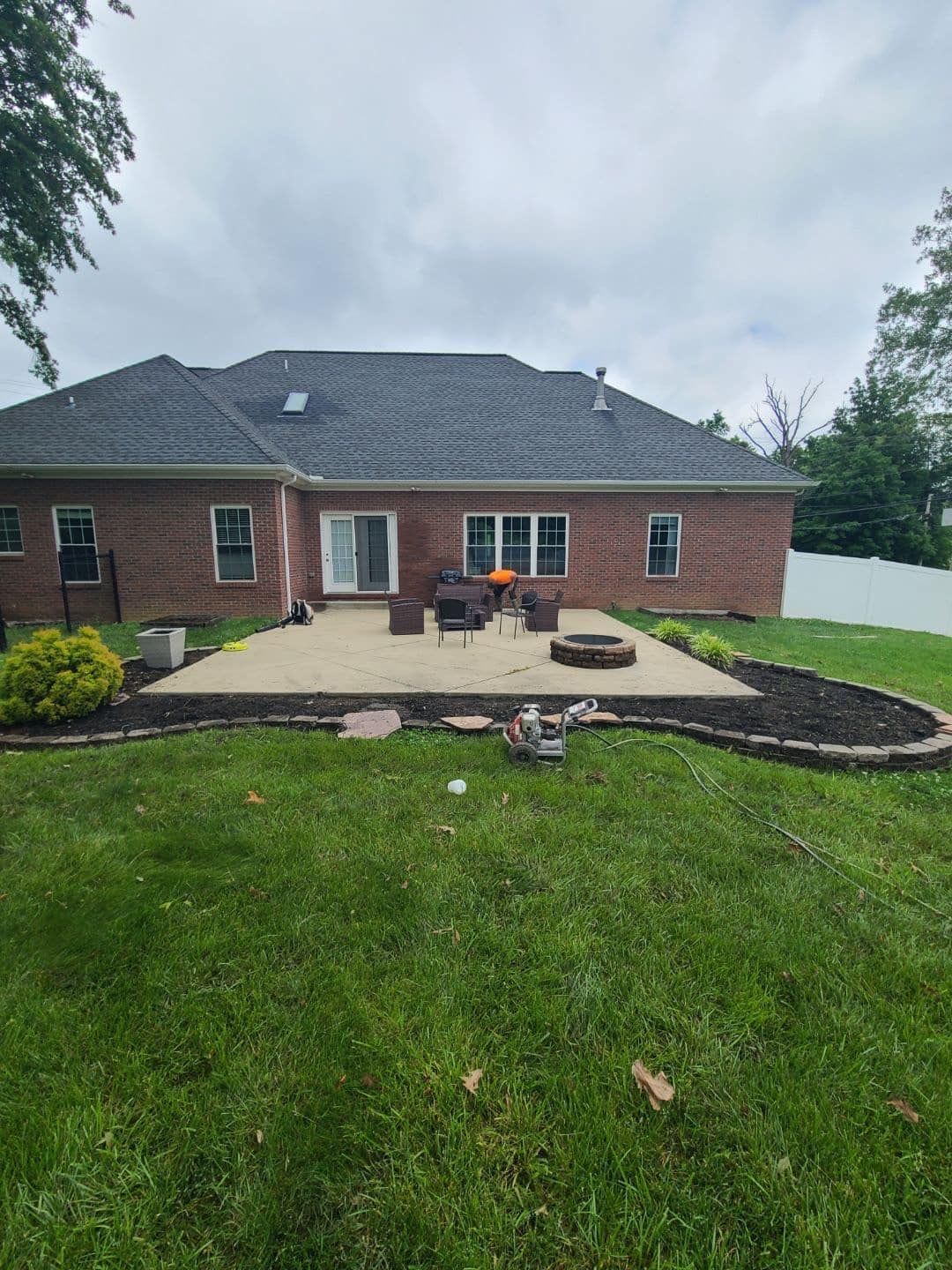 Backyard patio with fire pit, seating, and brick house under a cloudy sky.