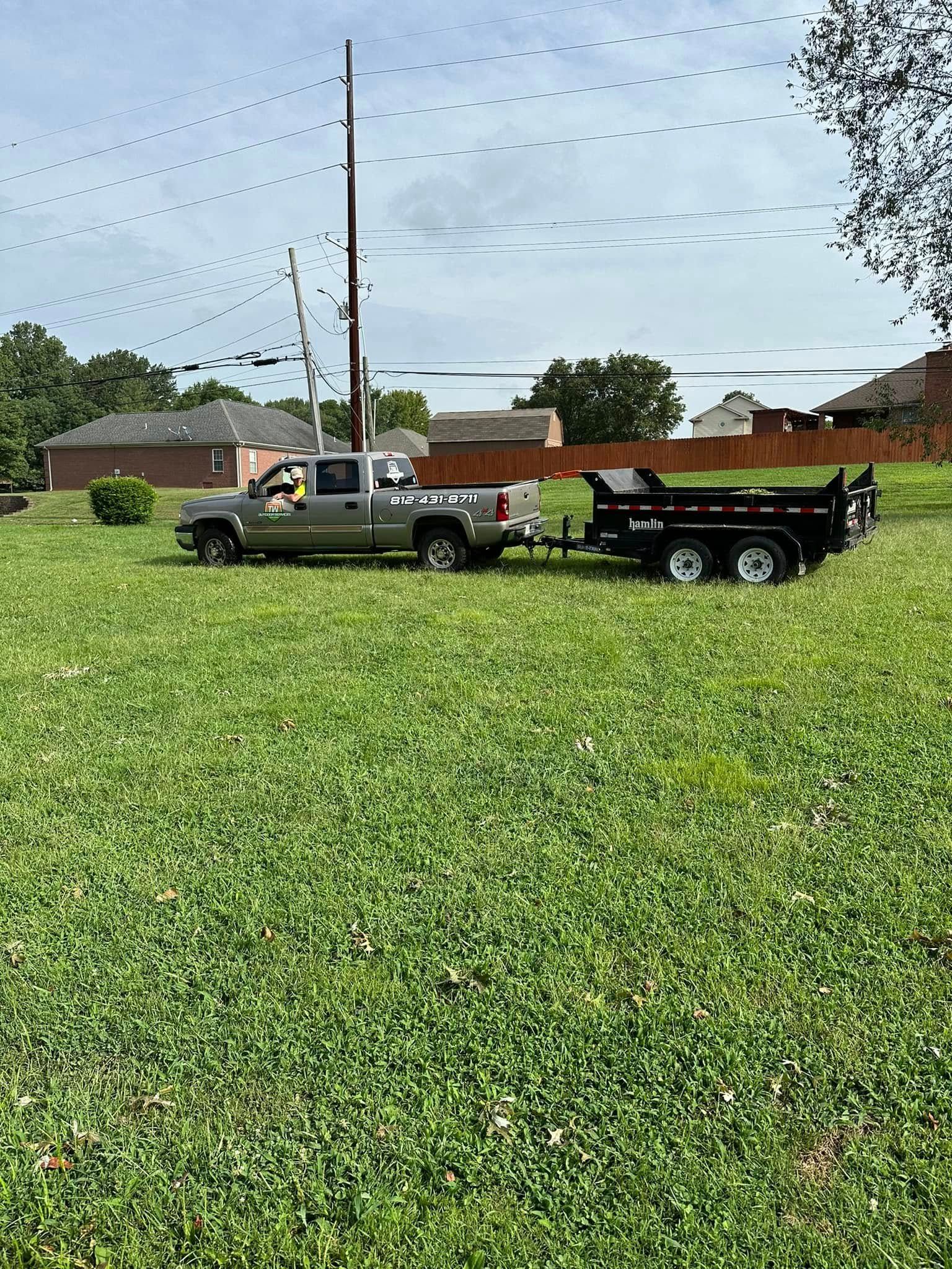 Truck with dump trailer on grass, under power lines. Person in truck cab.