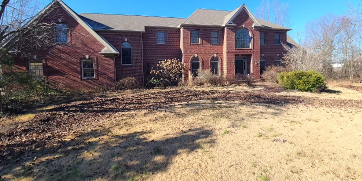 Large brick house with overgrown yard, clear blue sky.