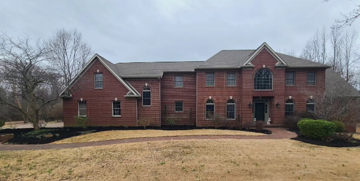 Two-story red brick house with a dark roof and arched window above the front door.