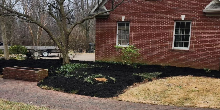 A red brick building with white-framed windows, surrounded by black mulch and a small brick planter.