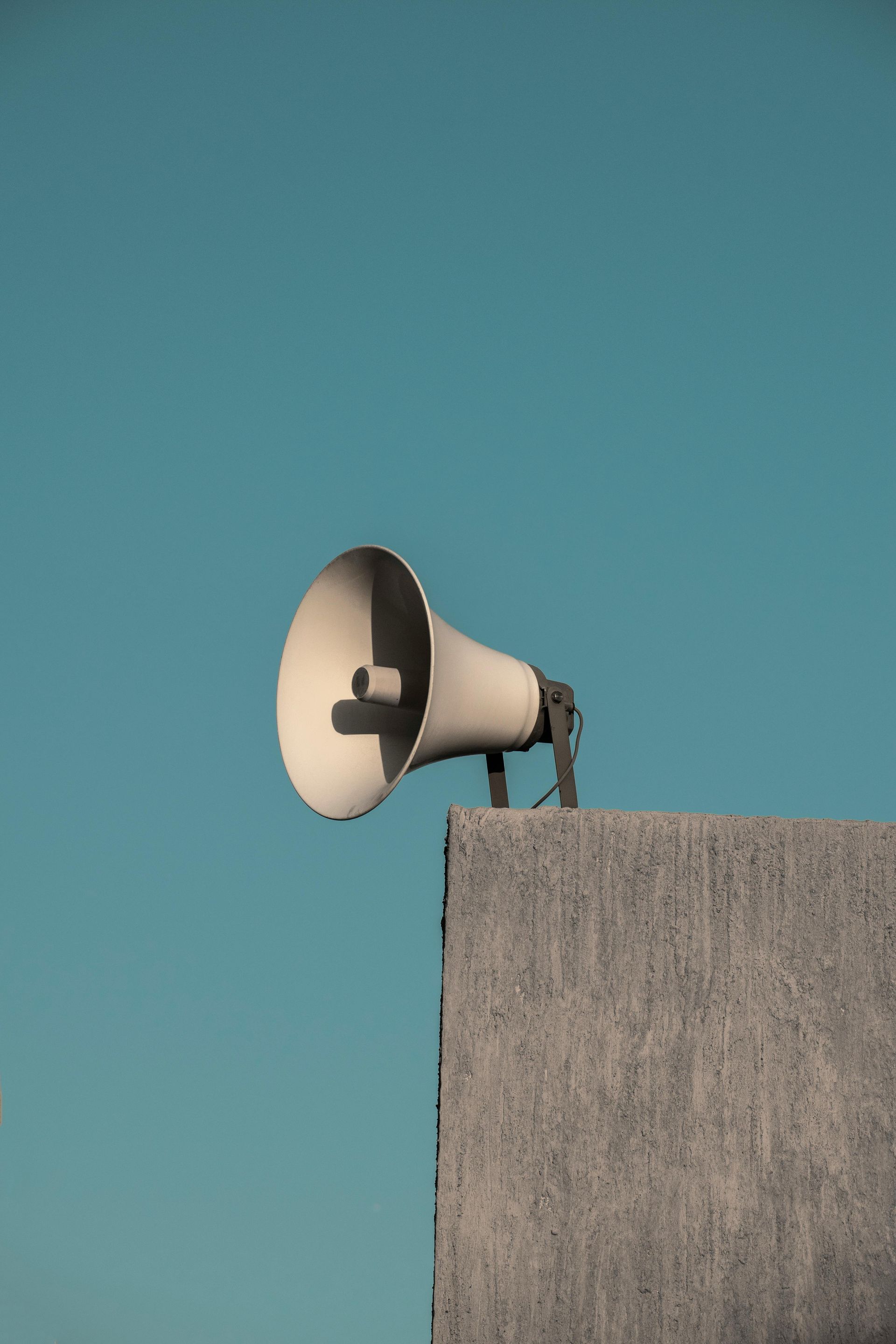 White megaphone mounted on a gray concrete structure against a teal sky.