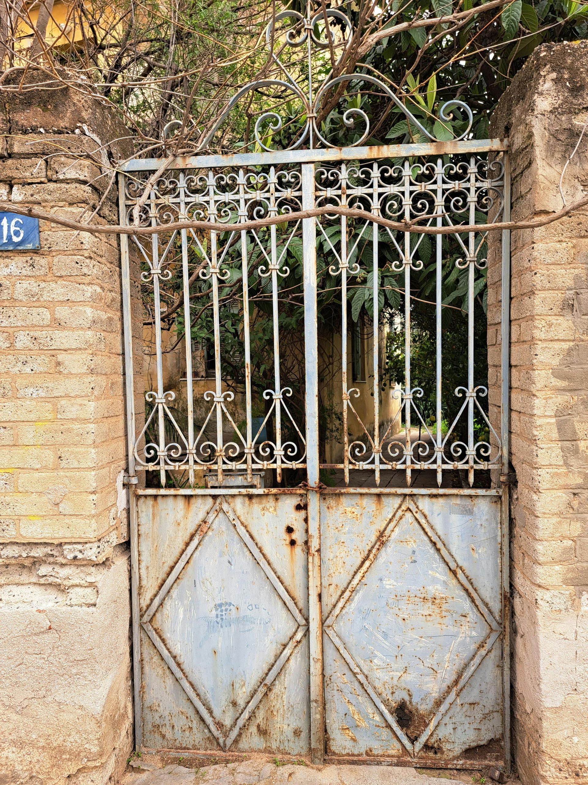 Rusty, ornate metal gate in brick wall. Blue number 
