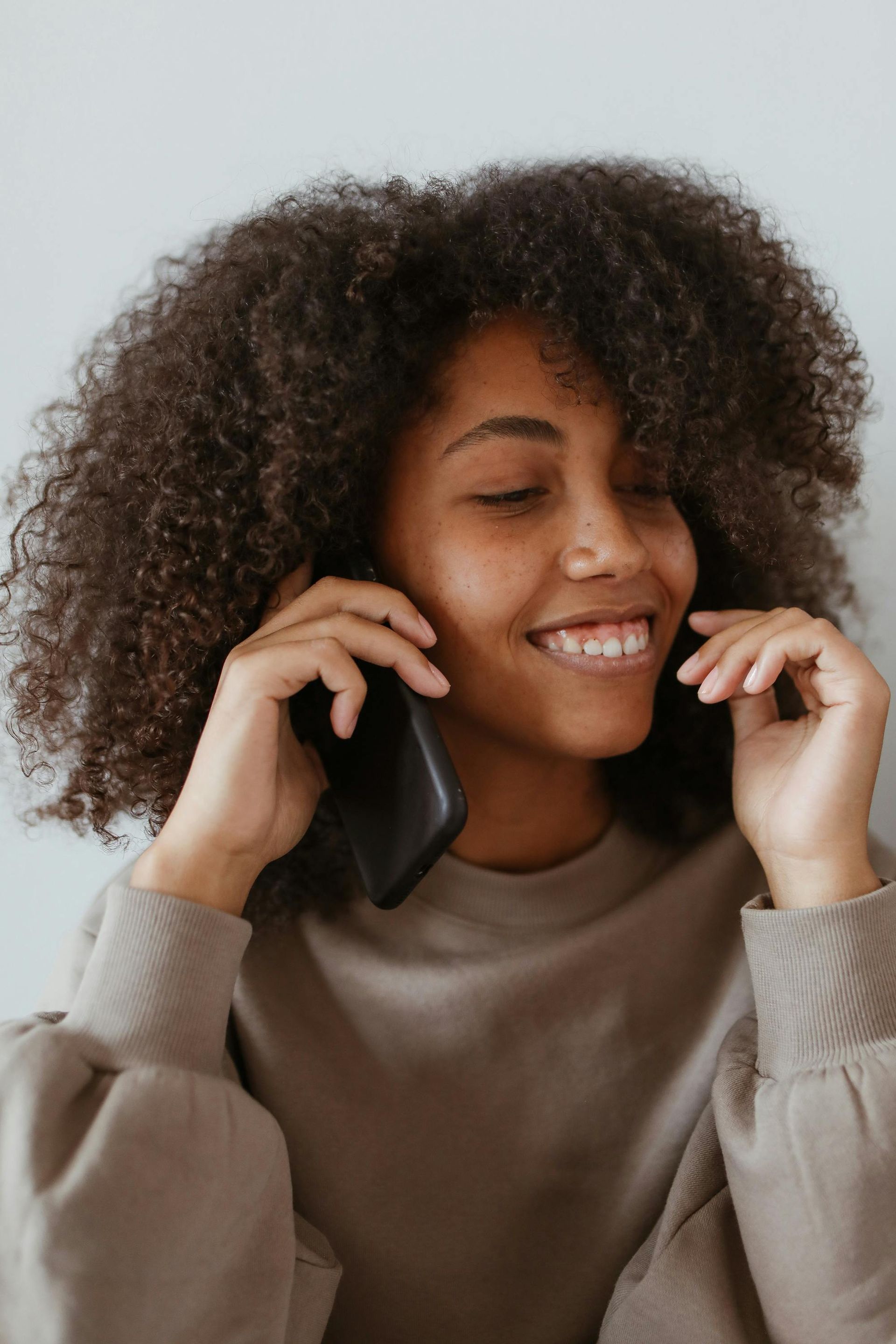 Woman with curly hair smiling while talking on a cell phone.