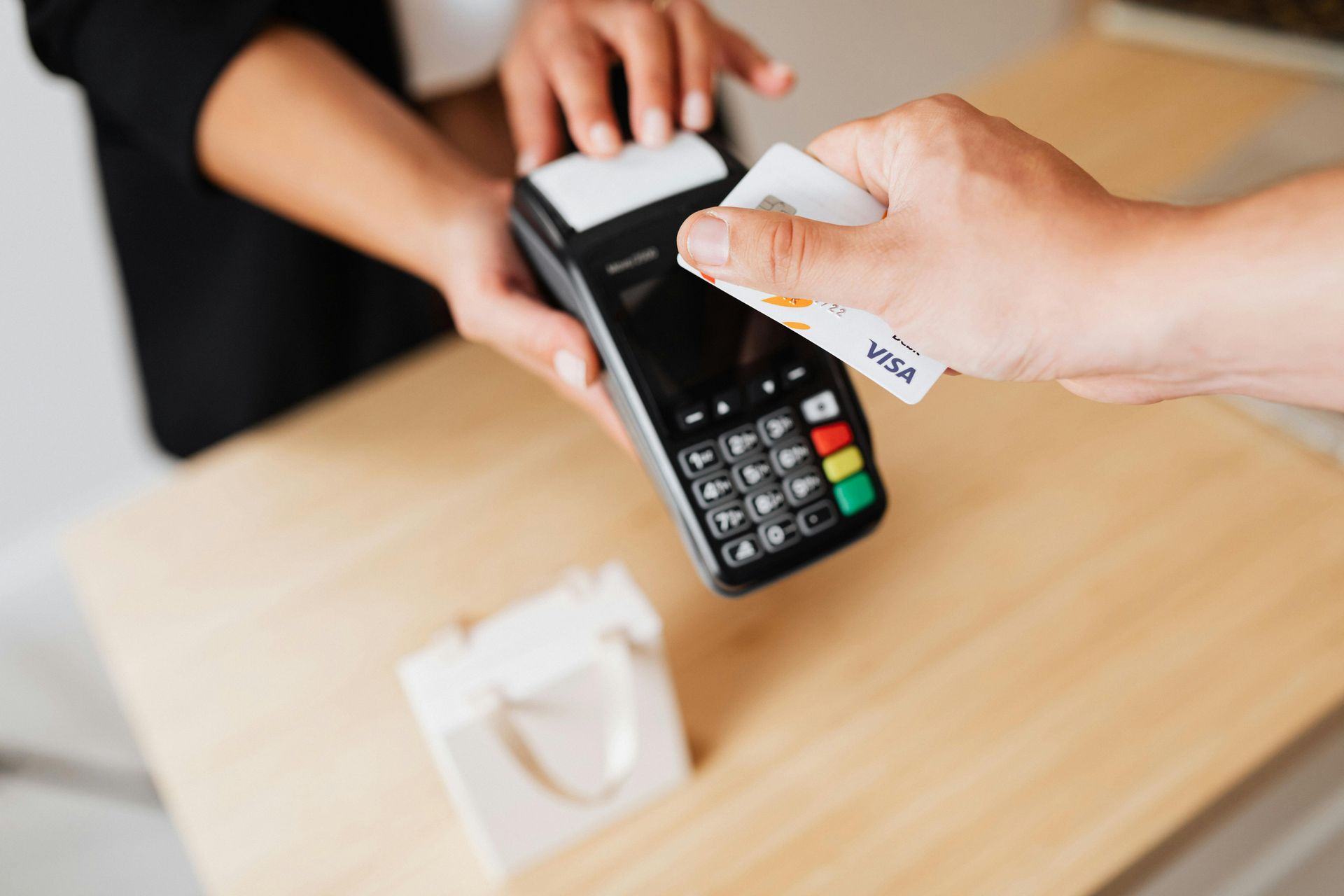 Person paying with a credit card at a payment terminal on a wooden counter.