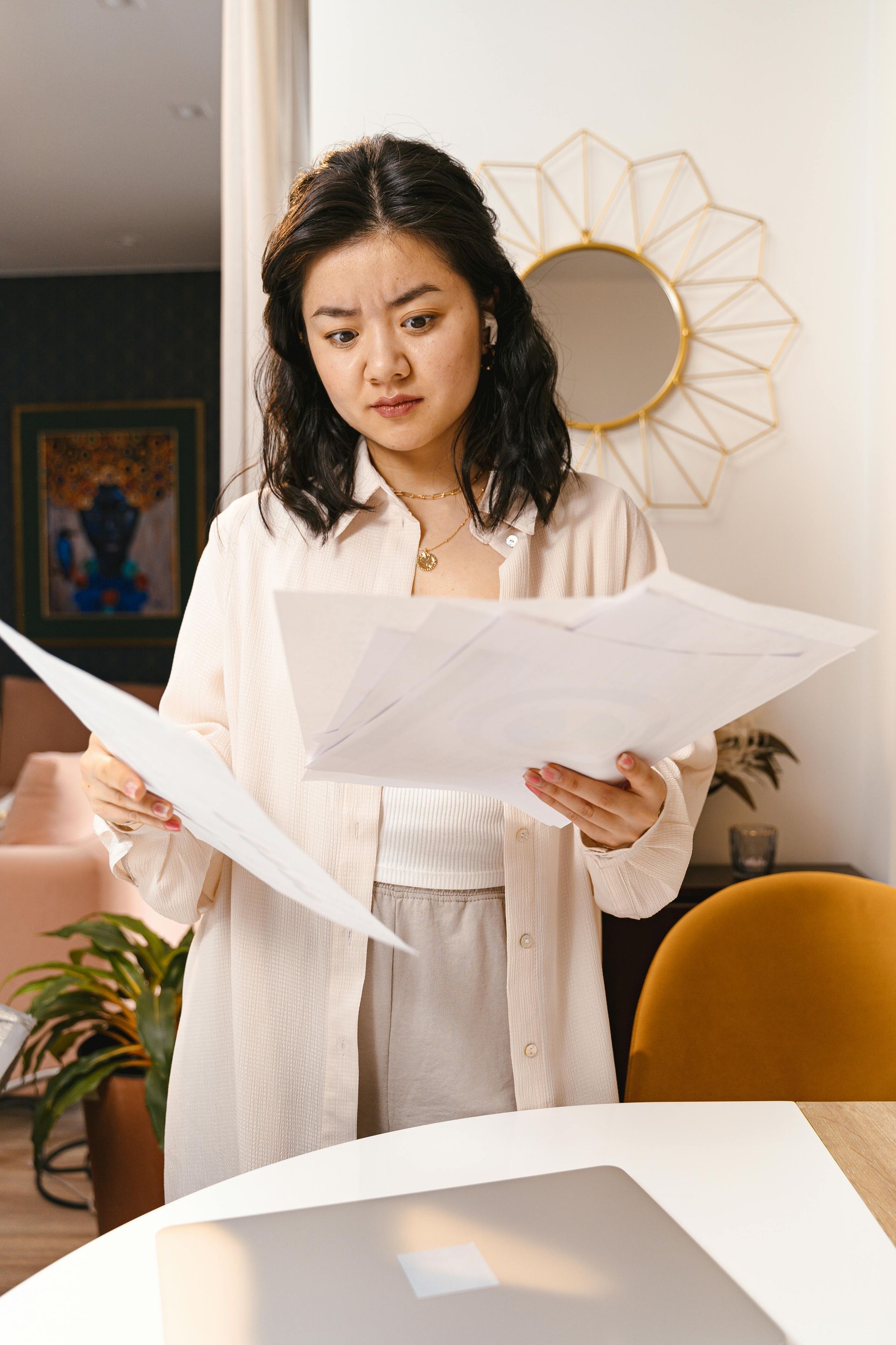 Woman looking at papers, possibly confused, in a home office setting.