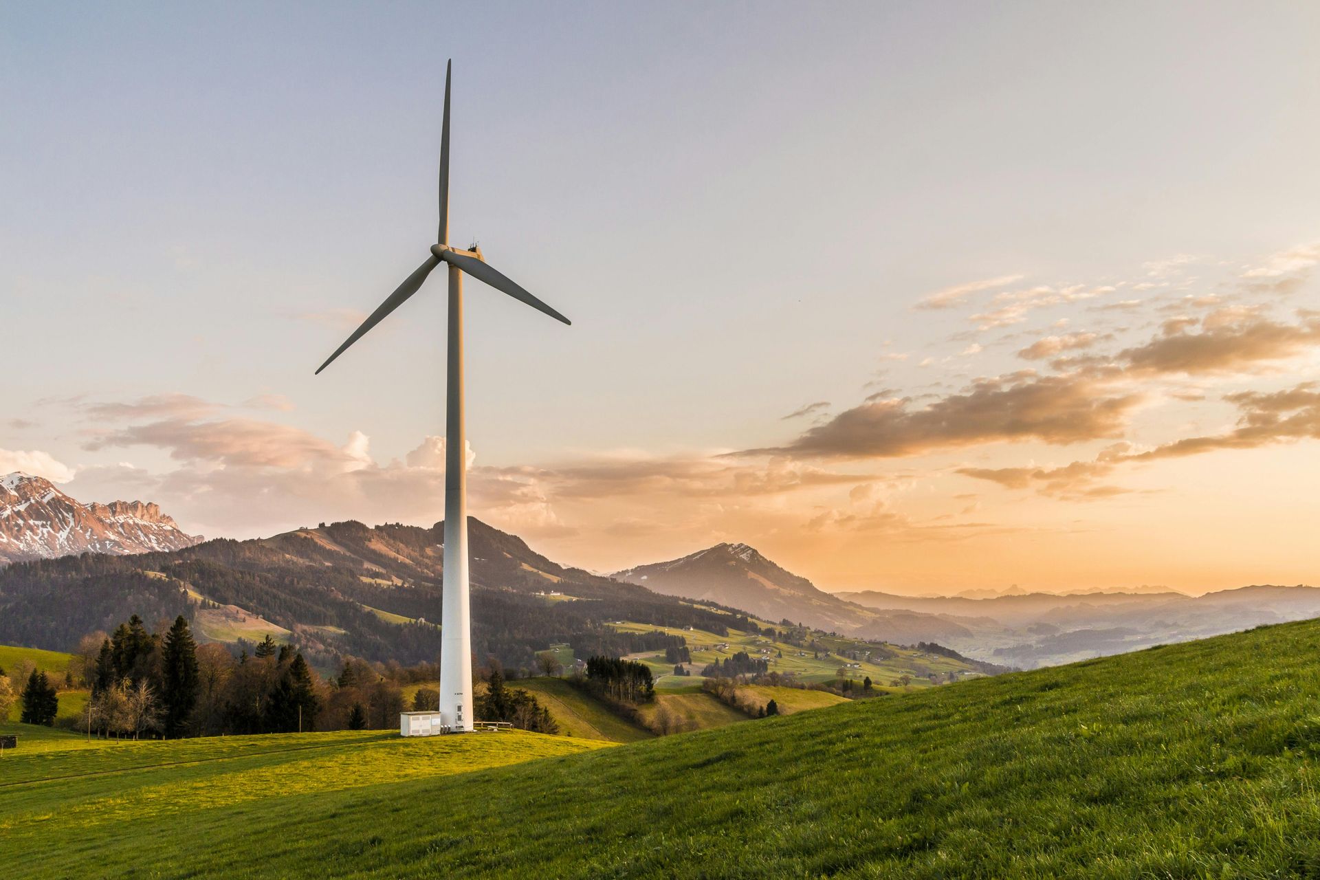 A wind turbine in a grassy field with mountains in the background