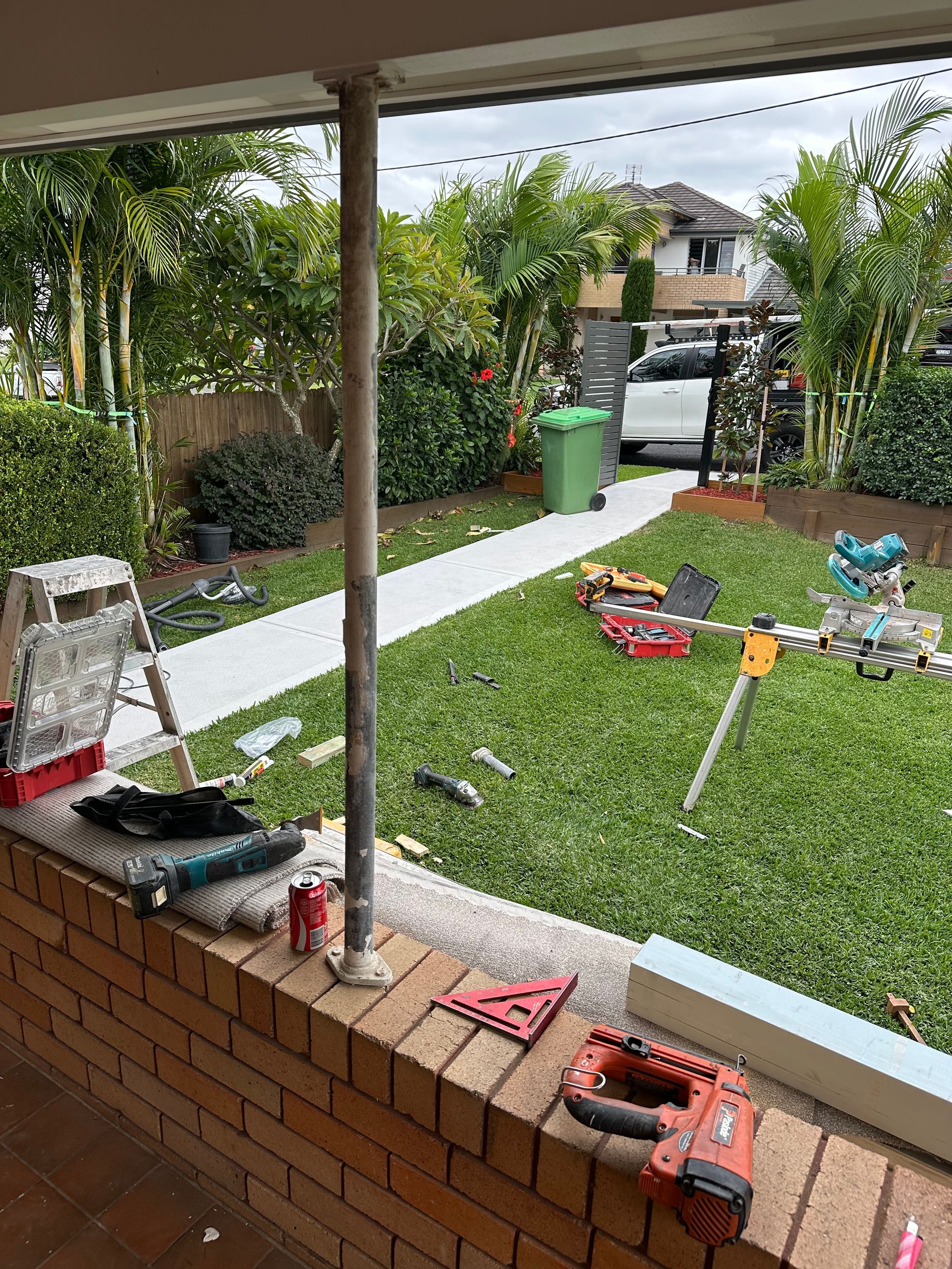 Construction tools and equipment are scattered across a brick patio and a lawn in a residential backyard.