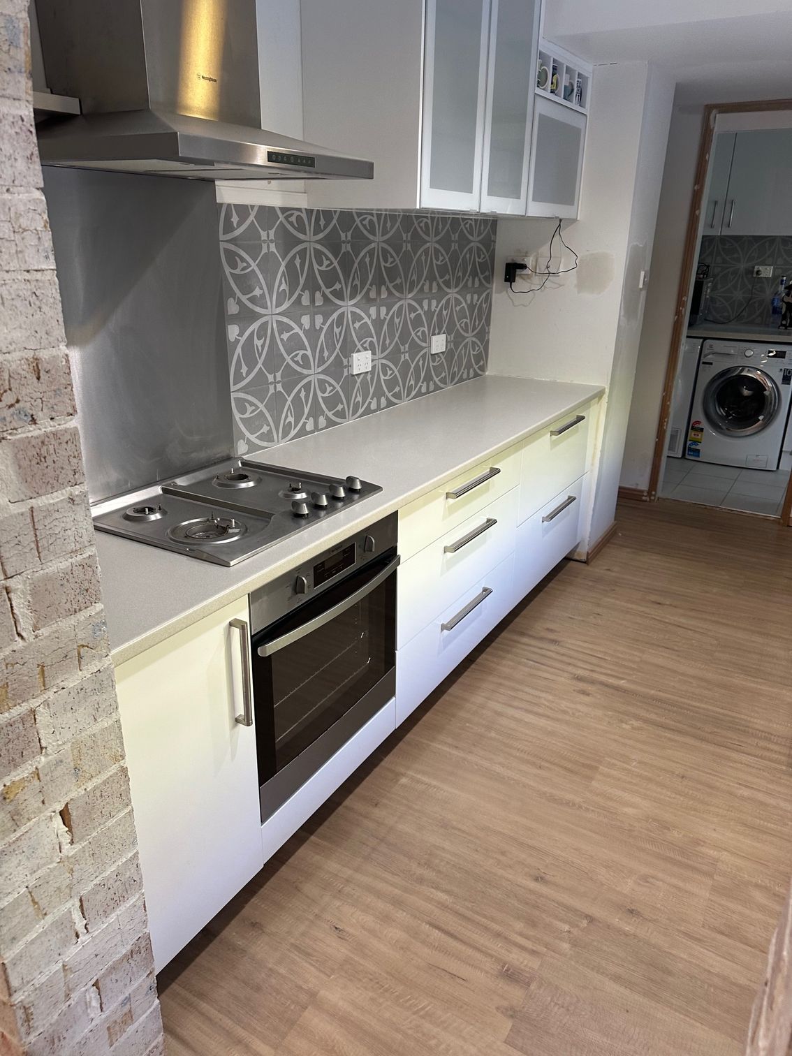A modern galley kitchen with white cabinets, light countertops, a patterned grey backsplash, and a stainless steel oven.