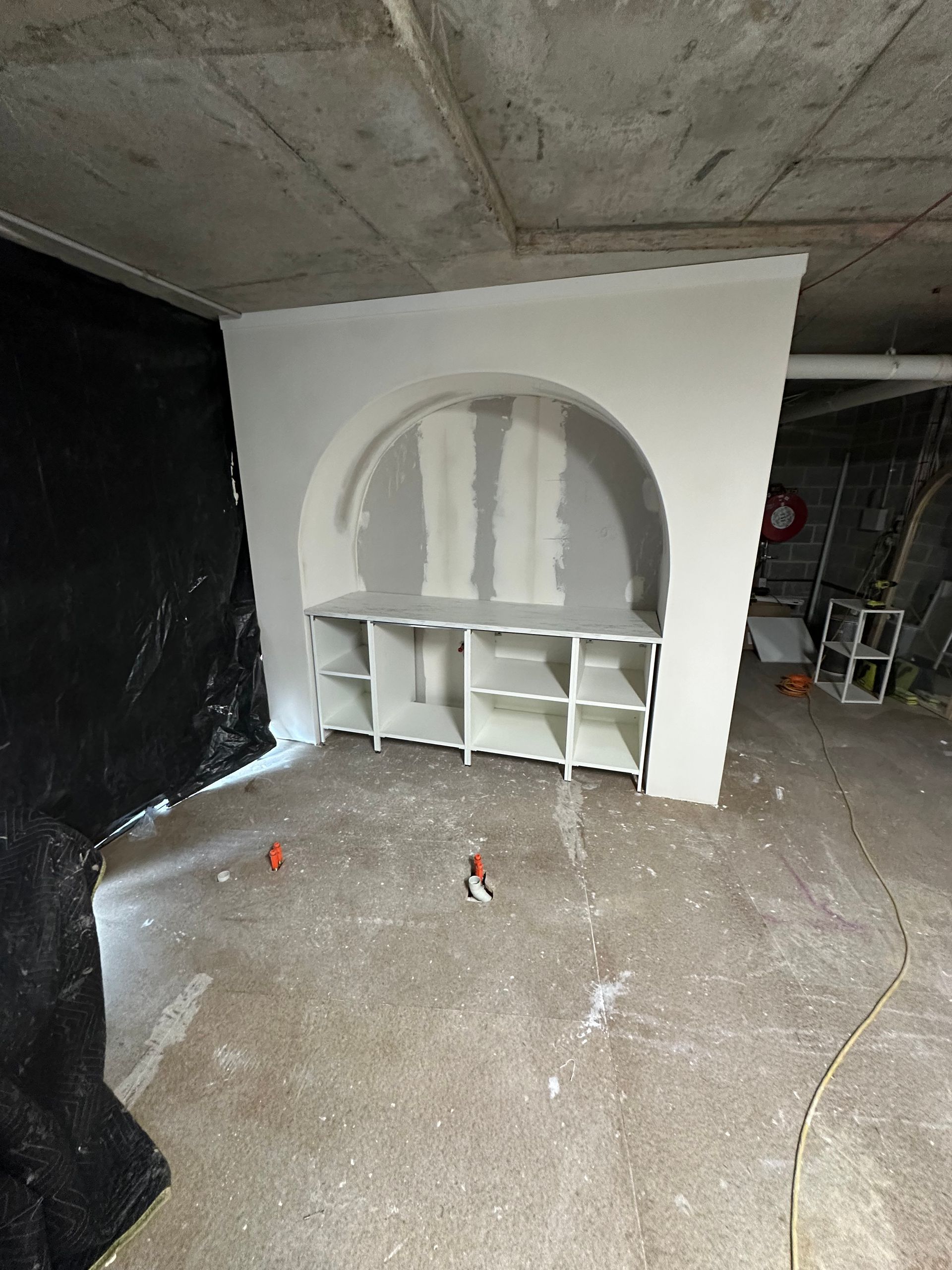 An arched alcove with built-in white shelving stands in an unfinished, industrial room with a concrete floor.