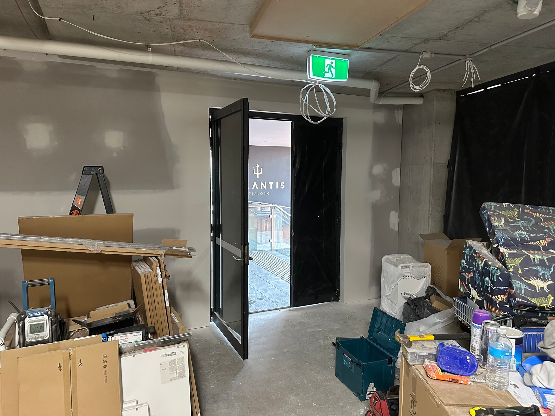 An open doorway leads to a patio, flanked by construction materials, cardboard boxes, and tools inside an unfinished room.
