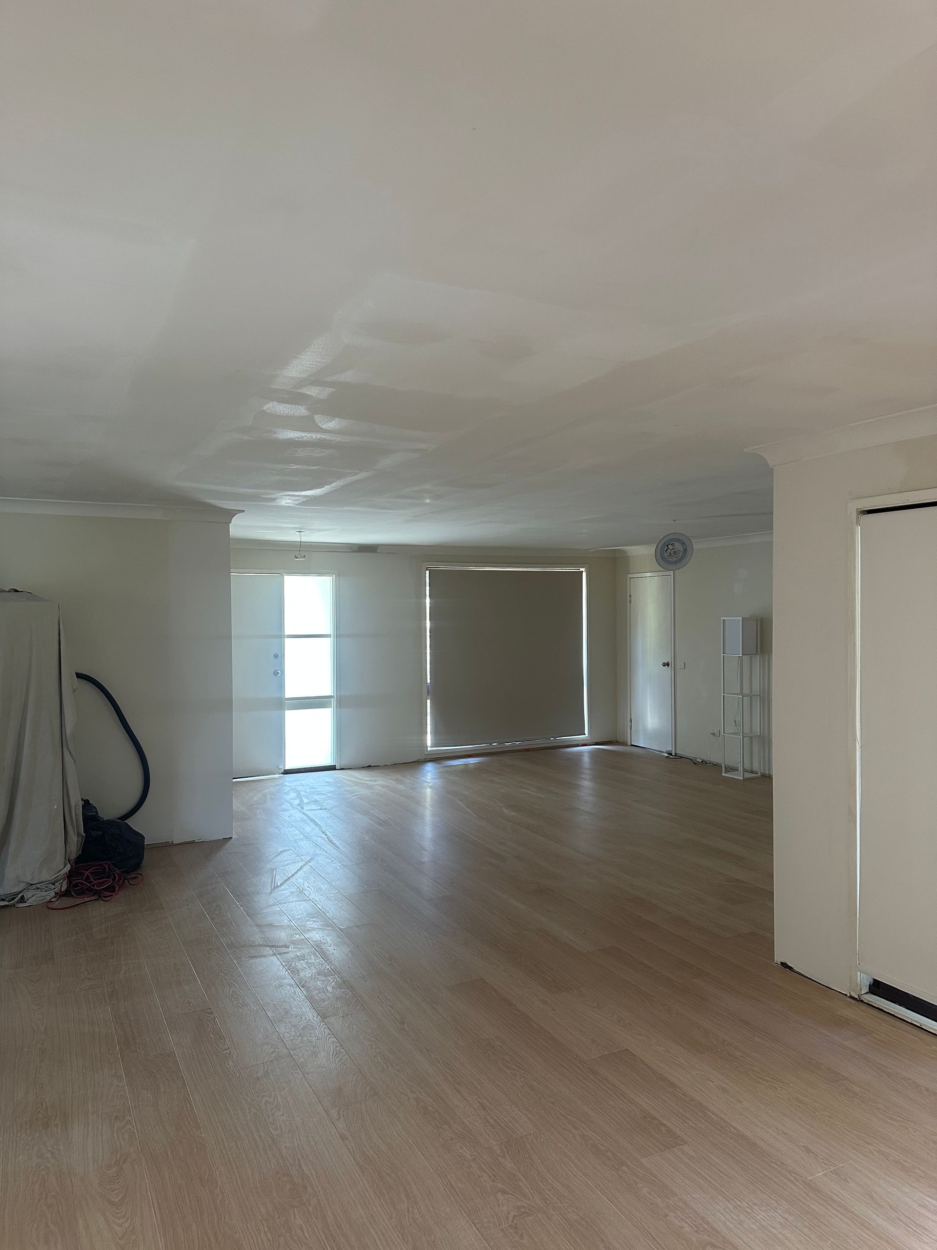 An empty, renovated room with light-colored flooring, white walls and ceiling, and a large window with a blind.