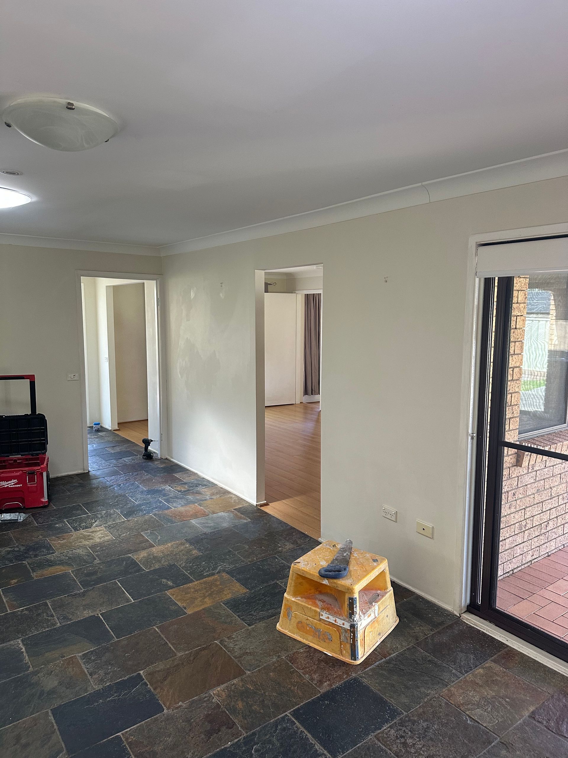 A room with dark slate tile flooring, off-white walls, two doorways leading to other rooms, and a square box on the floor.