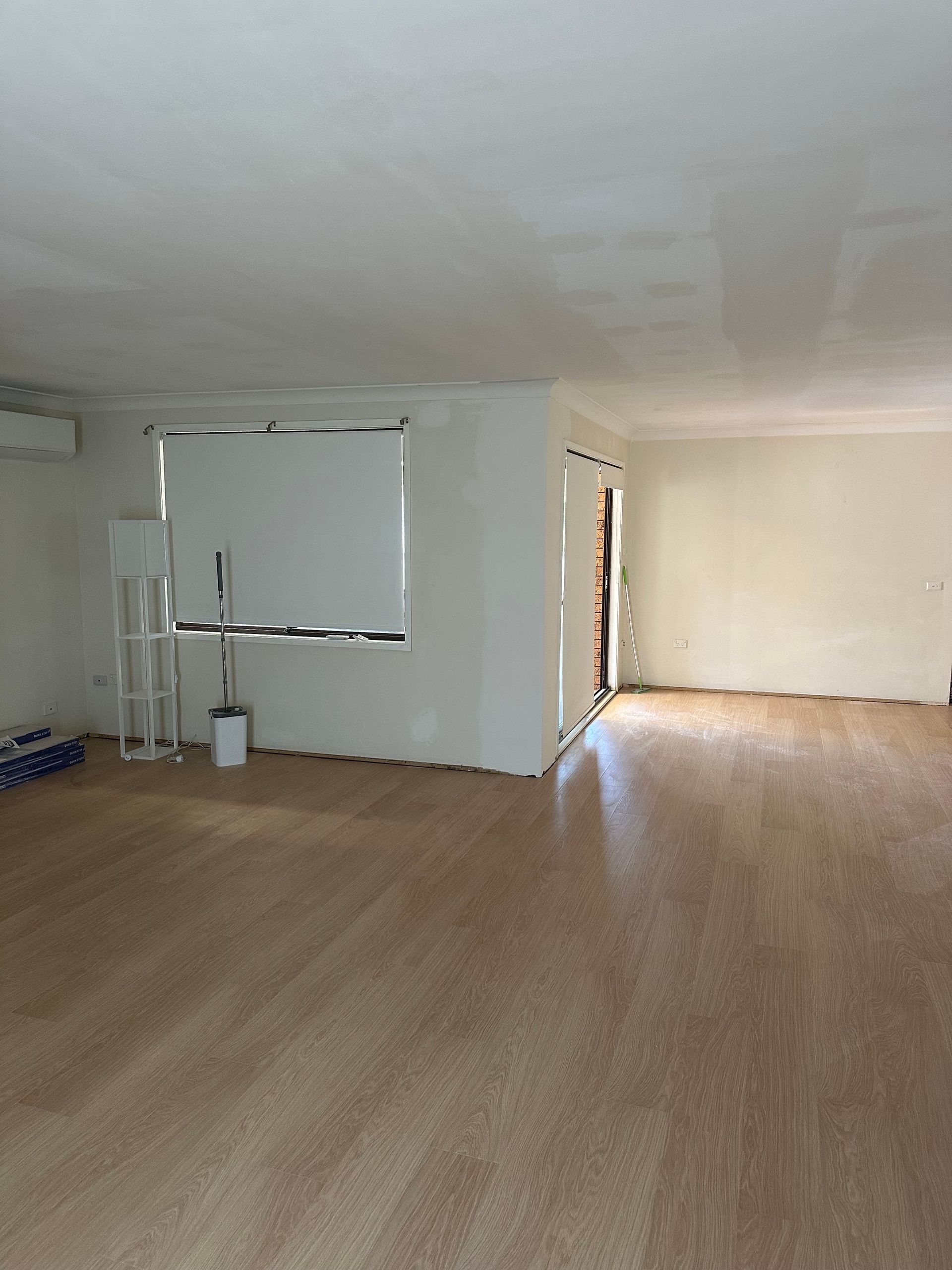 An empty, renovated room with light wood-look flooring, freshly painted white walls, a large window, and an open doorway.