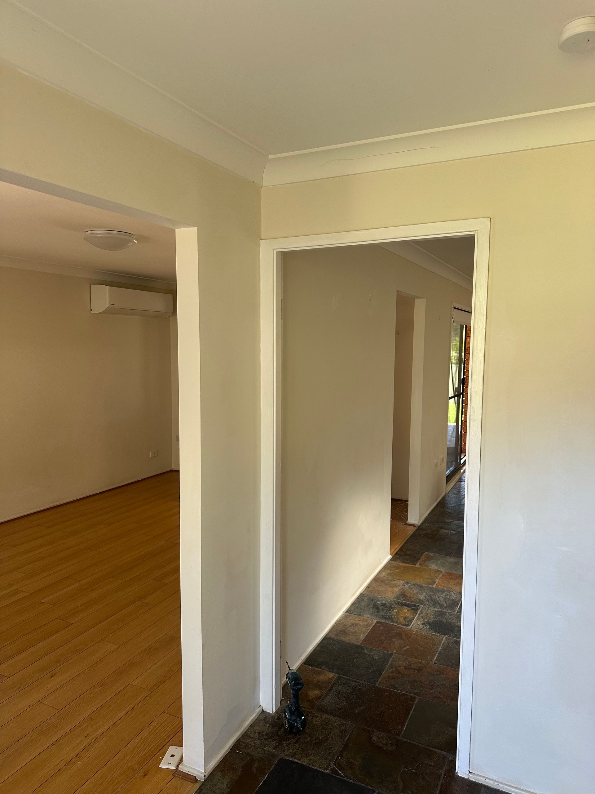 An interior view of a home showing an open doorway with a hallway leading to another room with light wood flooring.
