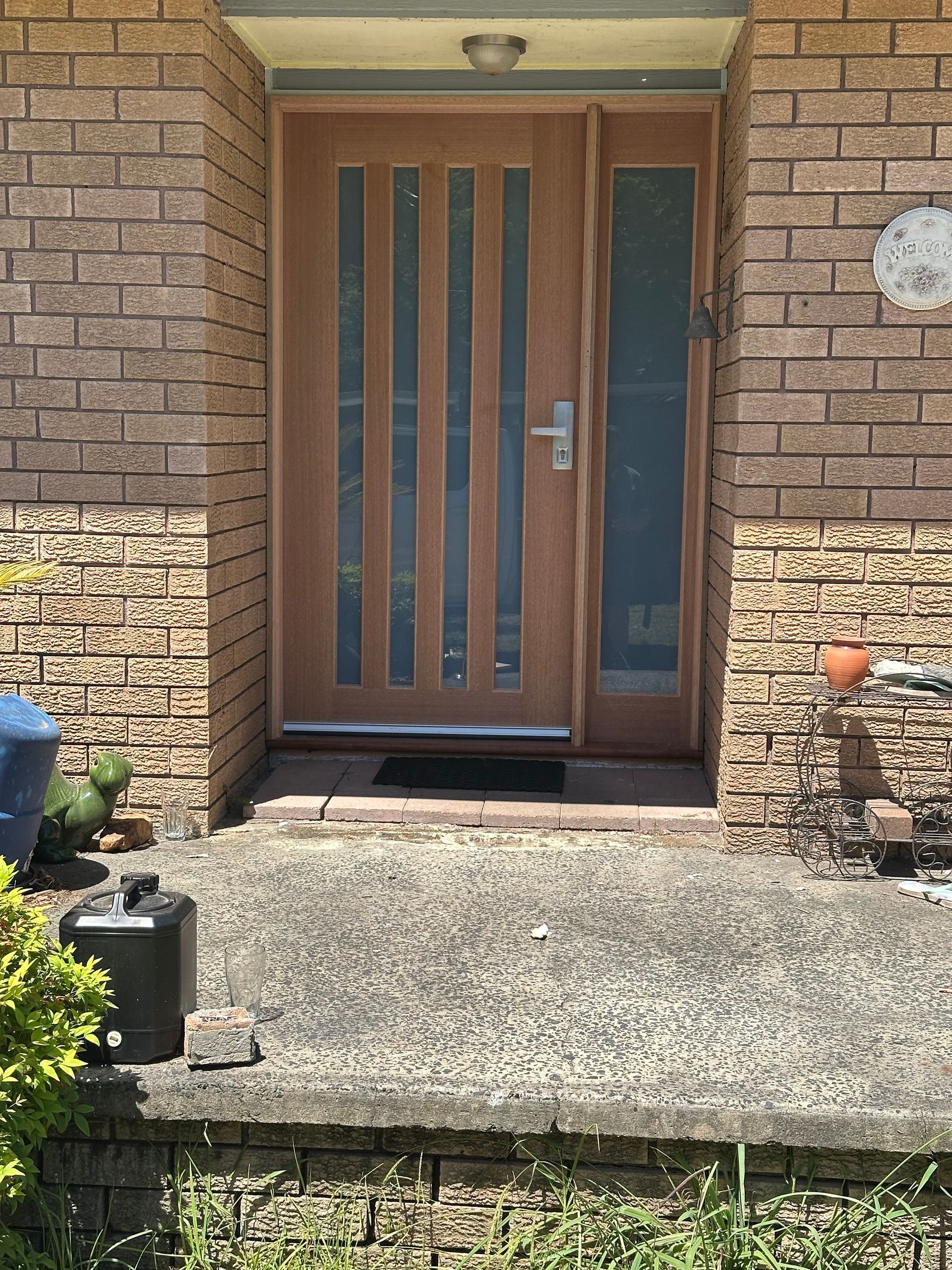 A modern wood-paneled front door with vertical glass inserts and a side window, framed by a tan brick exterior.