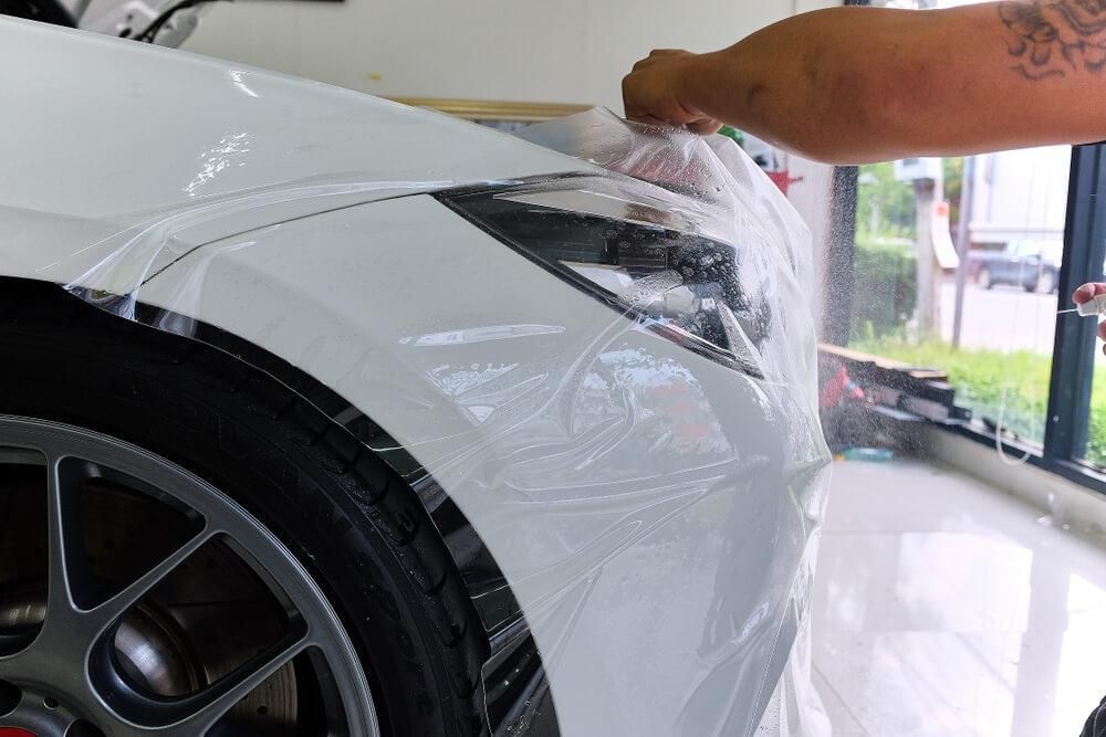 A person is wrapping a white car with plastic wrap.
