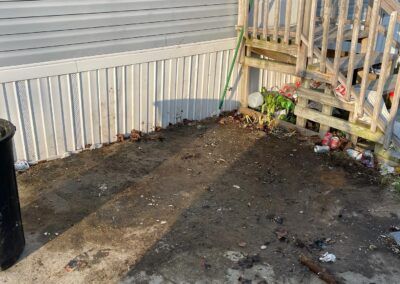 Muddy outdoor area with debris and stairs leading to a porch next to a light colored building.