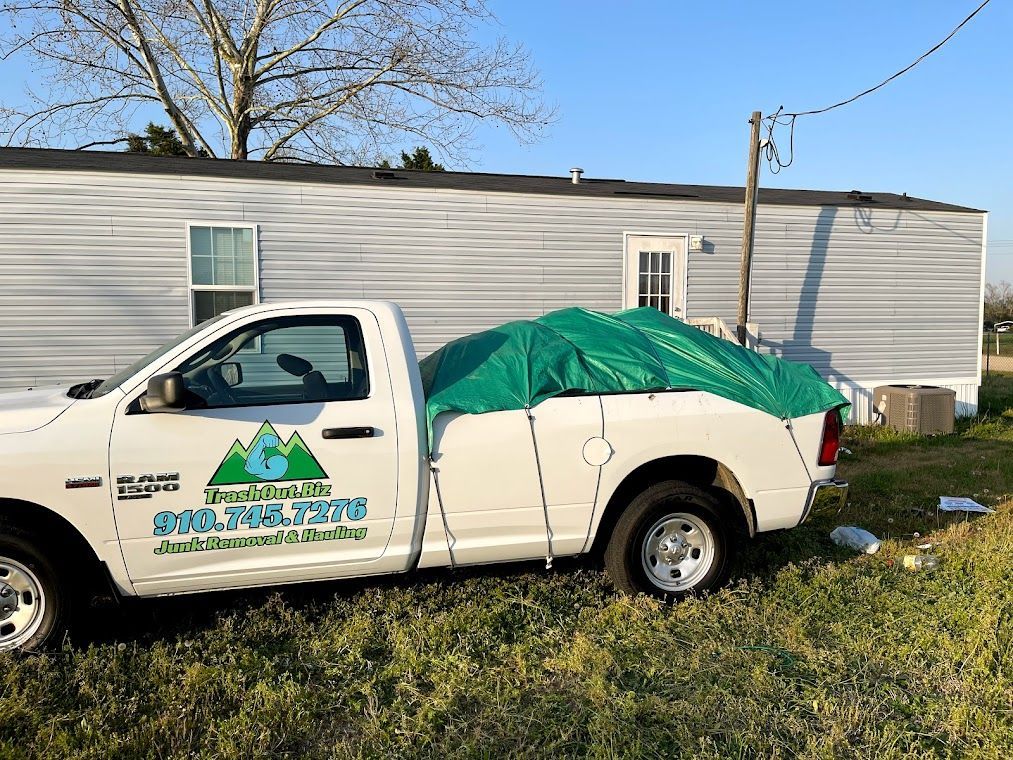 White truck with green tarp in bed, logo on side, parked in front of a mobile home.
