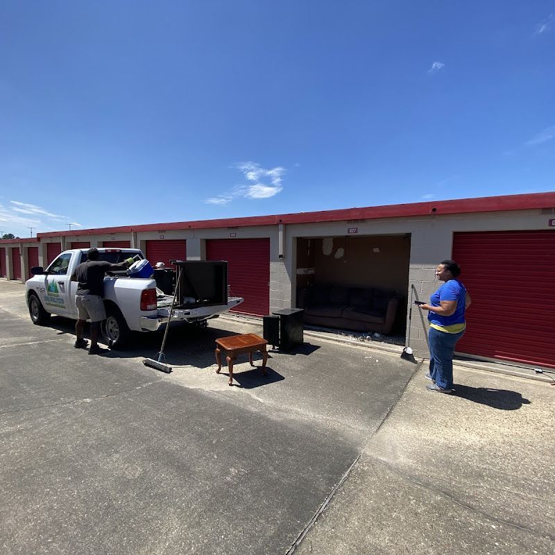 People unloading furniture from a truck into a storage unit on a sunny day.