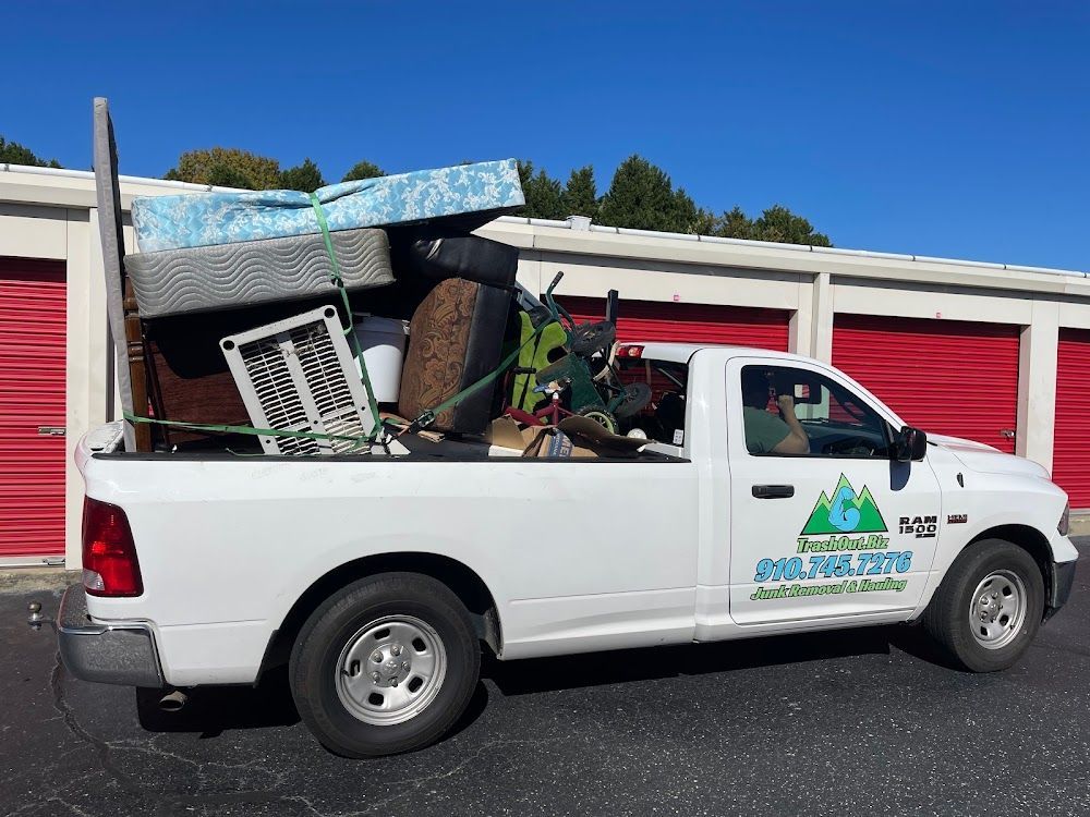White pickup truck loaded with furniture and items in front of red storage units under a blue sky.