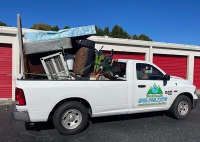 White pickup truck loaded with junk in front of storage units.